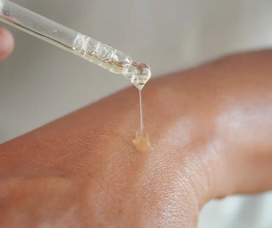 Close-up of a person using a dropper pipette to apply a skincare serum onto the back of their hand.