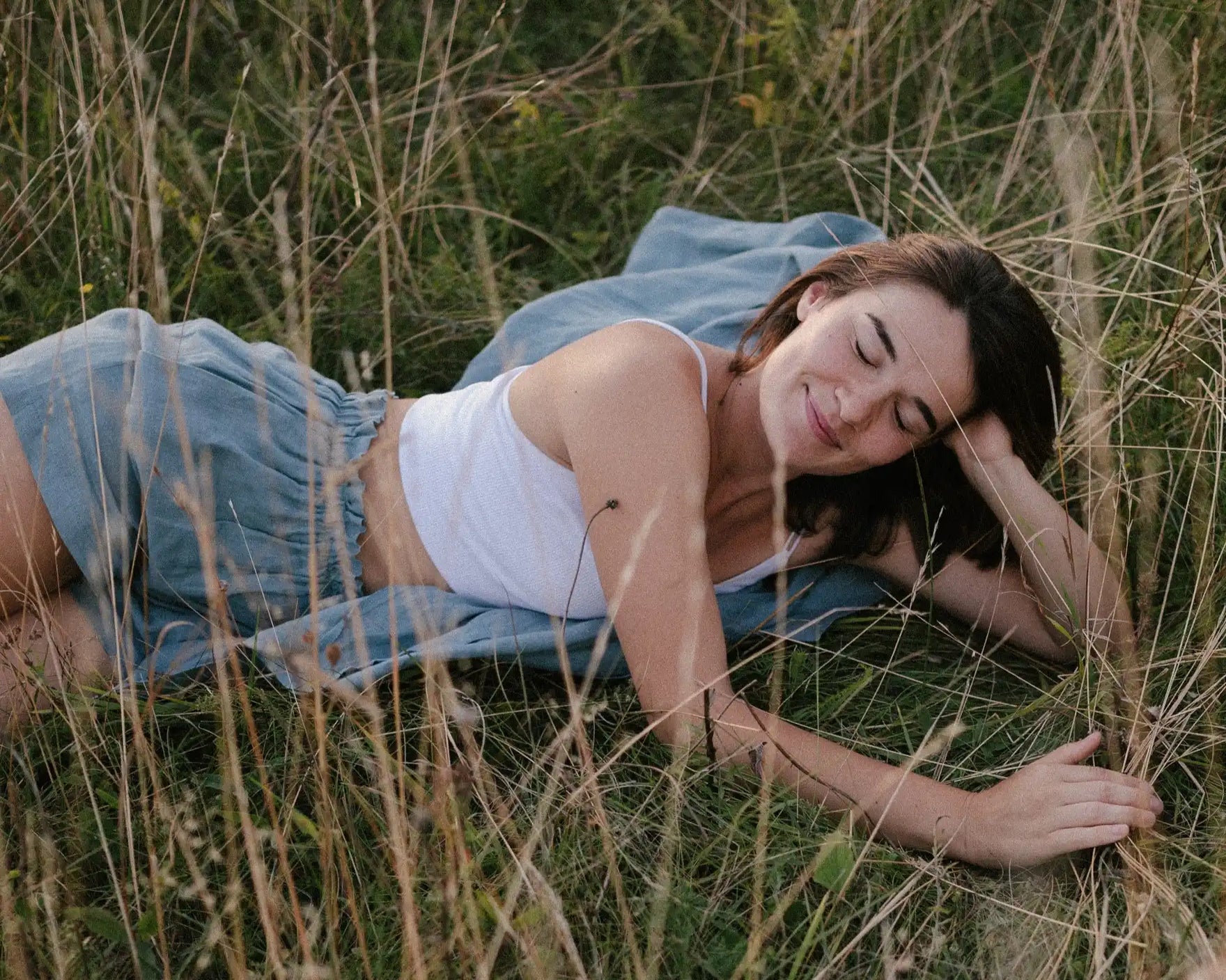 Woman lying in tall grass in natural light, relaxed summer mood