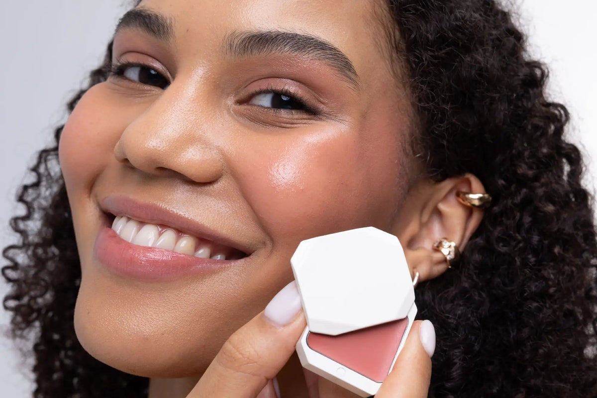 Smiling model holding Uoga Uoga cream blush compact in Blooming shade against unretouched skin