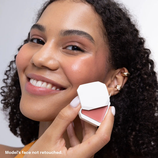 Smiling model holding Uoga Uoga cream blush compact in Blooming shade against unretouched skin