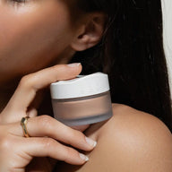 A close up of a woman holding Uoga Uoga Beach Mode bronzing powder jar next to her shoulder 