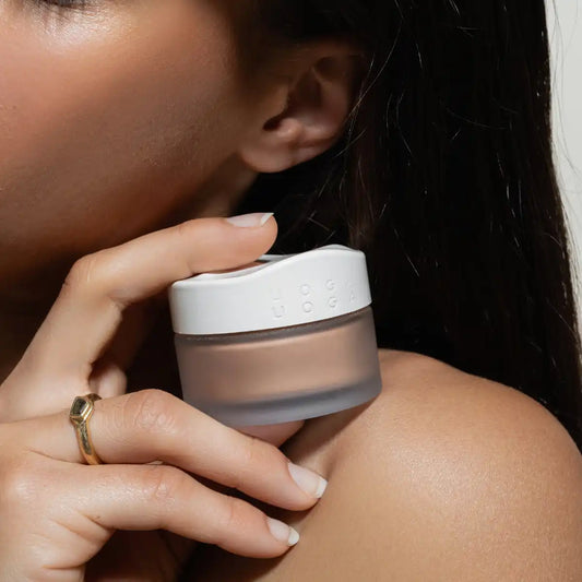 A close up of a woman holding Uoga Uoga Beach Mode bronzing powder jar next to her shoulder 