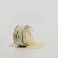 Jar of body scrub with a small amount spilled on a light grey background