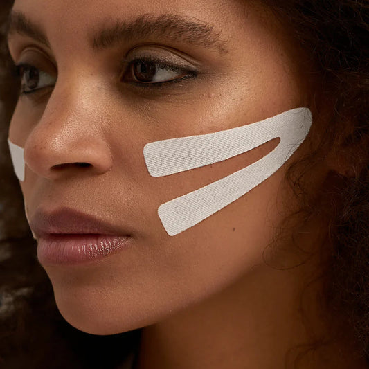 Close-up of a woman's face with white lines on her cheek against a dark background