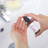 Hands dispensing Clémence & Vivien Sérum Perfecteur de Peau from its amber glass bottle onto a palm