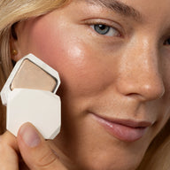 Close-up of woman holding Uoga Uoga Luminous cream highlighter next to her cheek