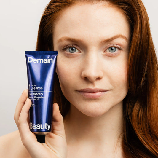 Femme rousse tenant le baume démaquillant Time to Detox de Demain Beauty près de son visage