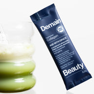 Demain collagen supplement sachet next to a glass with matcha on a white background