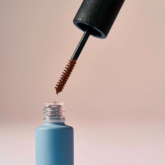 Eclo Warm Brown mascara with black applicator brush and blue tube on gradient background