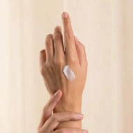 Hand with a small amount of Eclo Regenerating Hand Balm on the palm against a beige background