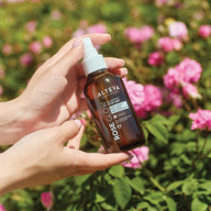 Hand holding a bottle of Alteva Rose Glow product with flowers in the background