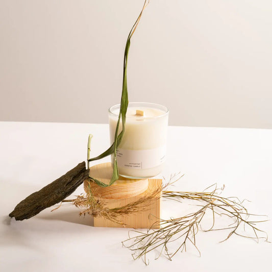 Hetkinen Archipelago Candle in a glass holder on a wooden block with dried plants on a light background