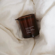 Amber glass jar containing a massage candle with visible label text, displayed on a white fabric background.