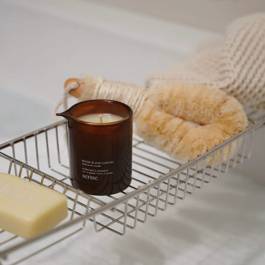 Massage candle from Sense Soulspace, soap, and loofah on a metal bath caddy with a blurred background