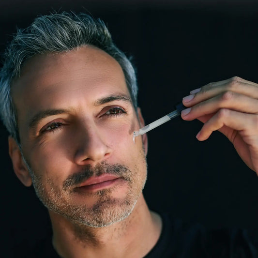 Close-up of a man applying the Glacier Revital Face Serum to his cheek against a dark background.
