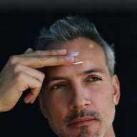 Close-up of a man applying Jungkraut Mountain Supreme Intense Cream to his forehead against a dark background.