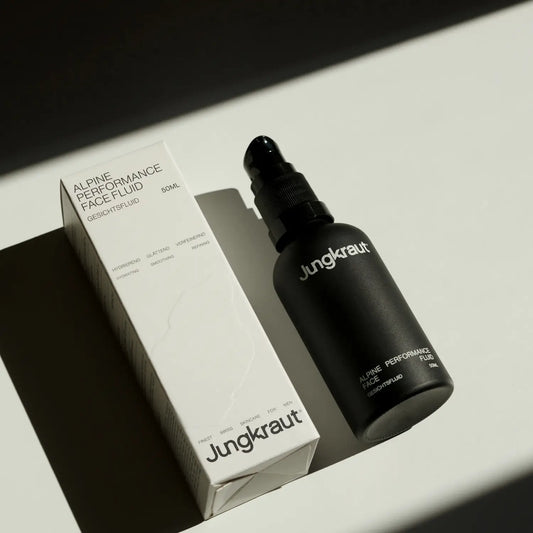 Jungkraut Alpine Performance Face Fluid in a black glass bottle with a nozzle dispenser, shown next to its outer cardboard box on a white background.