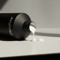 Black bottle labelled 'Jungkraut' pouring Wild Forest Body Lotion onto a light grey surface.