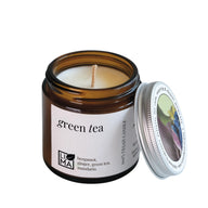 Green tea candle in a brown glass jar with a white label on a white background