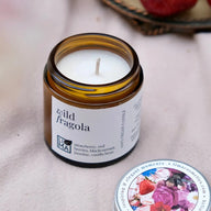 Candle in an amber jar labelled "Wild Fragola", surrounded by strawberries on a light background