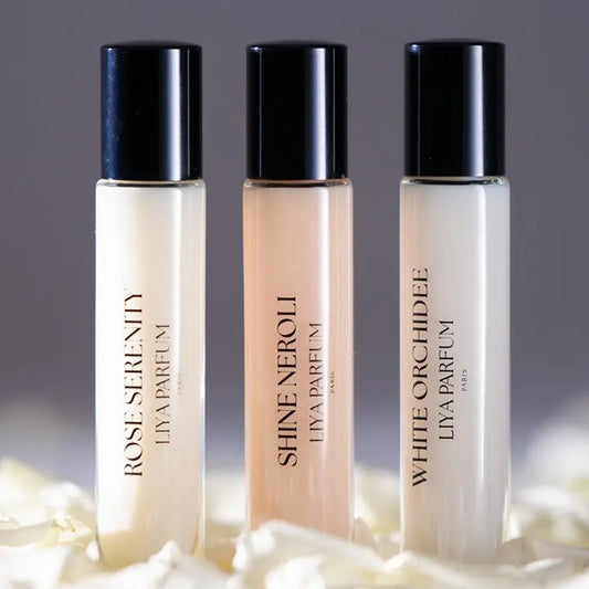 Three Liya Parfum Paris bottles displayed on a base decorated with flower petals.