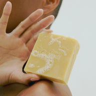 Hand holding Lost Alhambra Soap with lather on a neutral background