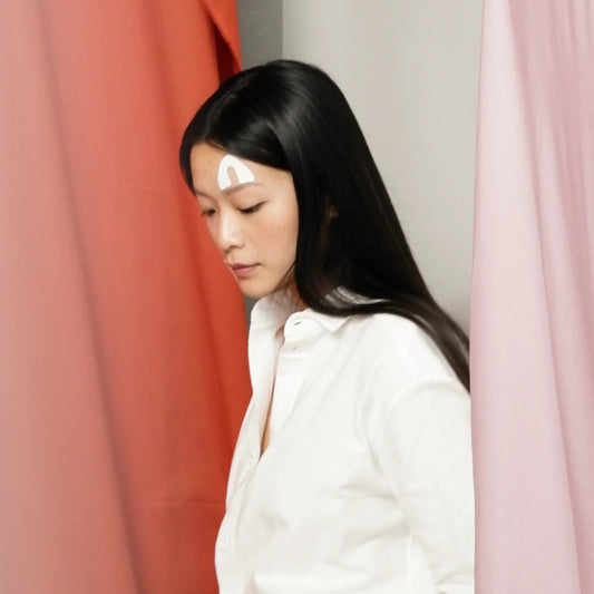 Woman wearing Lyfta forehead lifting kinesiology tape between colorful curtains