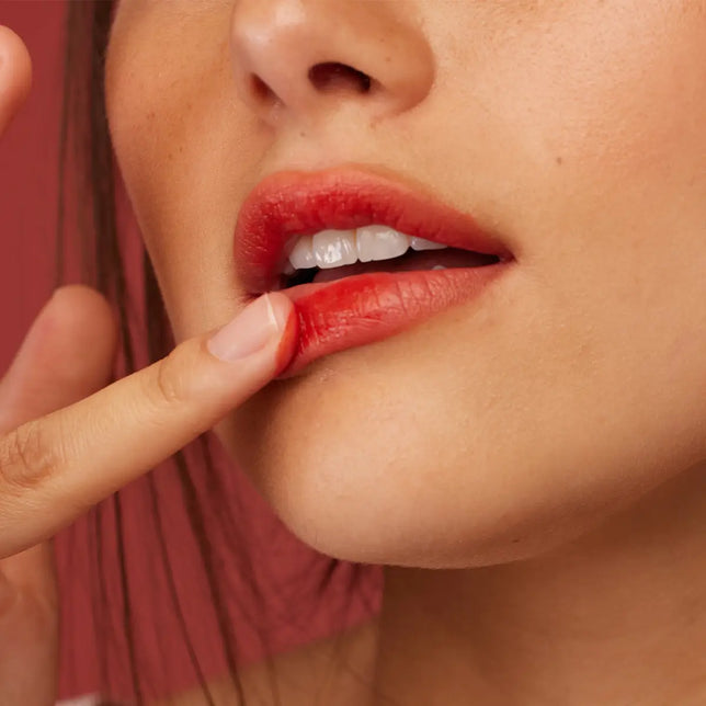 Close-up of a woman applying red Rouge Crush lipstick with a finger.