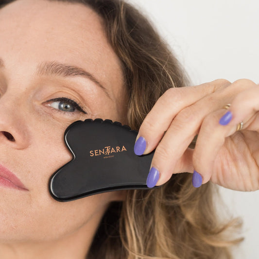 Woman holding a black gua sha tool with Sentara branding against a white background