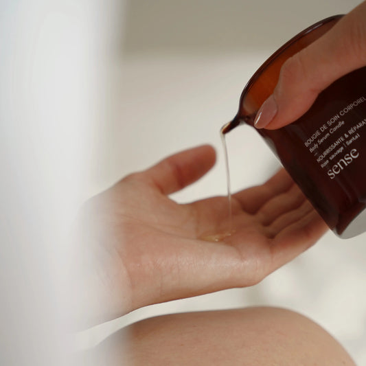 Hand pouring a warm nourishing massage candle oil from an amber glass jar onto skin.