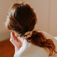 Person with a ponytail wearing Hydra Studio beige silk scrunchie against a neutral background