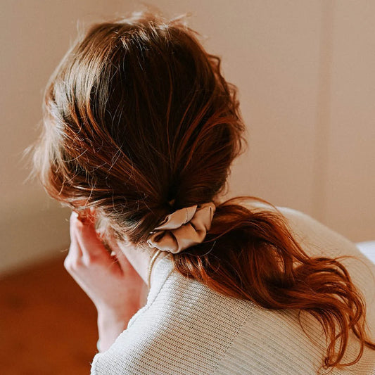Person with a ponytail wearing Hydra Studio beige silk scrunchie against a neutral background
