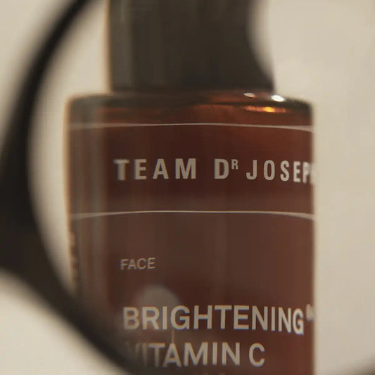 TEAM DR JOSEPH Brightening Vitamin C Serum amber bottle seen through a magnifying glass