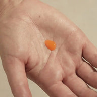 A drop of orange TEAM DR JOSEPH Brightening Vitamin C Serum in the palm of a hand, showing its lightweight gel texture