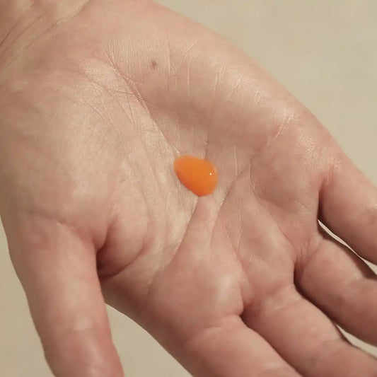 A drop of orange TEAM DR JOSEPH Brightening Vitamin C Serum in the palm of a hand, showing its lightweight gel texture