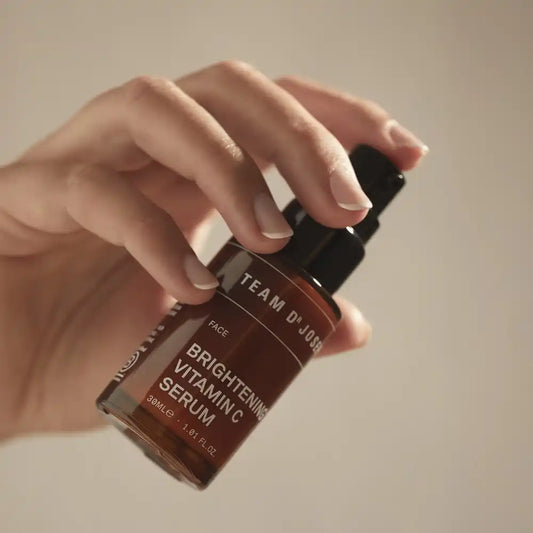 Hand pressing the pump of a TEAM DR JOSEPH Brightening Vitamin C Serum bottle