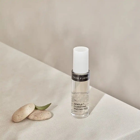 TEAM DR JOSEPH Gentle Clarifying Enzyme Peel with a white cap, beside smooth pebbles and a green leaf