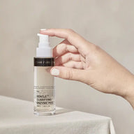 Hand pressing the pump of a TEAM DR JOSEPH Gentle Clarifying Enzyme Peel 50 ml bottle on a linen-covered table