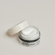 Open jar of TEAM DR JOSEPH Supreme Well Aging Cream showing the white cream texture, with the wooden lid resting against it