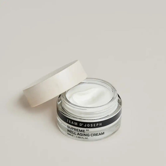 Open jar of TEAM DR JOSEPH Supreme Well Aging Cream showing the white cream texture, with the wooden lid resting against it
