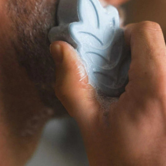 Hand using UMAI blue shaving foam bar with lather on skin