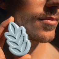 Person holding UMAI blue leaf-shaped shaving foam close to their face