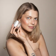 Woman holding Uoga Uoga Highlighter Game of Lights against her cheek on a neutral background