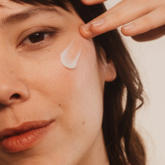 A woman applying Umai Relipidante cream to her face with a neutral background