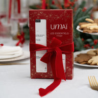 Red Umai Les Essentiels box with a bow on a festive table with cookies and candles