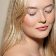 Close-up of a woman with blonde hair and pink lipstick against a neutral background