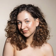 Woman with curly hair wearng Uoga Uoga Highlighter Game of Lights smiling against a neutral background