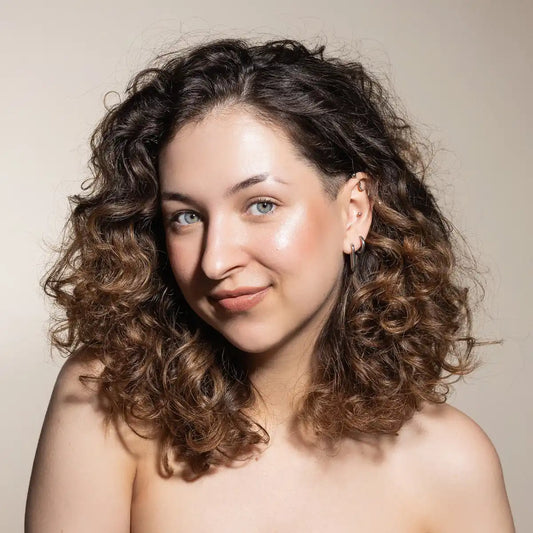 Woman with curly hair wearng Uoga Uoga Highlighter Game of Lights smiling against a neutral background
