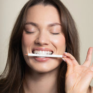 Woman holding Uoga Uoga lip pencil near her mouth with a neutral background
