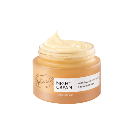 Open frosted amber glass jar of UpCircle Night Cream with hyaluronic acid and niacinamide, showing the swirled pale yellow cream inside.